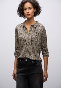 Camicia a bottoni con stampa leopardata in beige con macchie nere, maniche arrotolate, tessuto morbido, abbinata a jeans neri a vita alta.