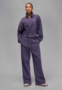 Paarse cropped sweatshirt met hoge hals en ritssluiting, gecombineerd met bijpassende wide-leg sweatpants. Voorzien van wit Jordan-logo op de borst.