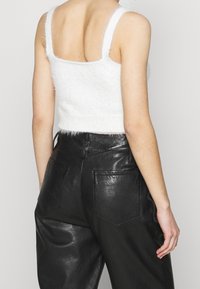 Top corto bianco e peloso con spalline larghe e piatte; abbinato a pantaloni neri in ecopelle a vita alta con due tasche posteriori.