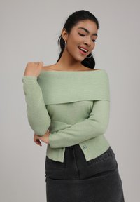 Light green off-the-shoulder sweater with ribbed texture and fitted sleeves, paired with a dark denim skirt featuring side pockets.