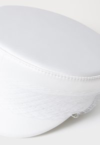 White cap made of smooth fabric with a rounded top, featuring a textured white netting detail along the side and subtle stitch accents.