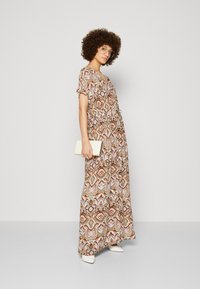 Maxiklänning i mönstrad tyg med jordnära toner, med korta ärmar och åtsittande midja. Matchad med vit clutch och skor.