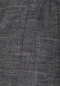 Tissu à carreaux gris et noir avec de fines lignes roses, tissage texturé, présentant une surface douce et de doux plis.