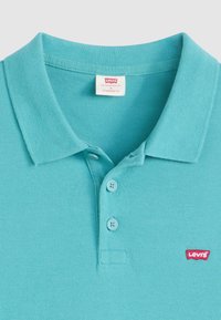 Tyrkysové polo tričko s textúrovanou látkou, s dvoma gombíkmi na légu a červeným logom Levi's na ľavej hrudi. Štandardný strih.