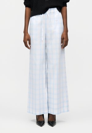 Asmuo dėvi šviesiai mėlynas ir baltas languotas plačias kelnės su raišteliu juosmenyje ir juodus aukštakulnius.