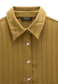 Musztardowa żółta koszula zapinana na guziki z wyraźnym kołnierzykiem, z cienkimi czerwonymi pionowymi paskami i teksturowanym materiałem. Pojawiają się cztery guziki.