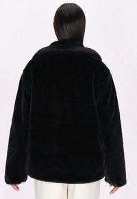 Sort faux fur-jakke med en afslappet pasform, brede ærmer og høj krave. Blød tekstur og ensfarvet, ingen synlige detaljer eller mønstre.