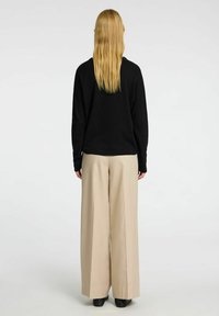 Černý pletený svetr a béžové kalhoty s širokými nohavicemi, pohled zezadu. Oblečení má volný střih a jemnou texturu s minimálním designem.