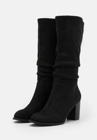 Bottes à talons en suède noir décontractées avec un talon bloc solide. Le design présente un bout arrondi et une tige douce et texturée.