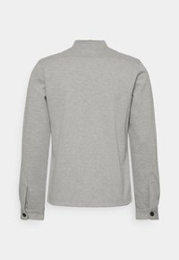 Chemise grise à manches longues en tissu doux. Dotée d'un col, de poignets boutonnés et d'un design arrière épuré sans motifs ni accents.