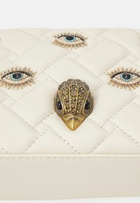 Borsa a tracolla in pelle color crema trapuntata con hardware decorativo a forma di uccello in oro e occhi impreziositi con dettagli turchesi e neri.
