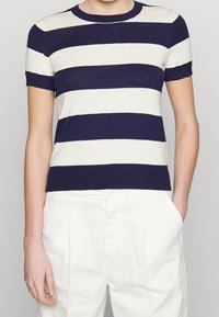 Námořnický a krémový pruhovaný krátký rukáv pletený top s kulatým výstřihem. Tkanina je lehká a hladká. V kombinaci s bílými kalhotami.