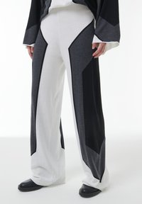 Wijduitlopende gebreide broeken met witte, grijze en zwarte geometrische kleurblokken, gedragen met zwarte schoenen en een bijpassend lange mouwen top.