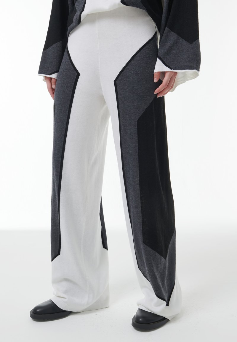 Wijduitlopende gebreide broeken met witte, grijze en zwarte geometrische kleurblokken, gedragen met zwarte schoenen en een bijpassend lange mouwen top.