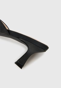 Black high-heeled shoe with a slim, curved heel and closed toe on a white background.