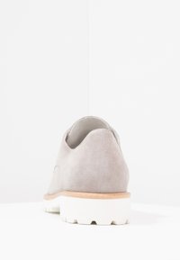 Scarpa in suede grigia con un retro arrotondato, suola in gomma e un elegante accentuazione marrone chiaro alla base, caratterizzata da una texture liscia e un design minimalista.