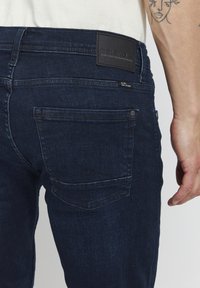 Jean en denim bleu marine avec une coupe droite, des poches arrière et une étiquette en cuir à la taille avec un logo en relief.