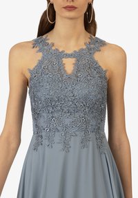 Hellblaues Kleid mit aufwendig floralem Spitzenmuster und einem Ausschnitt im Schlüsselhintern. Ärmelloses Design mit einem glatten, fließenden Rock.