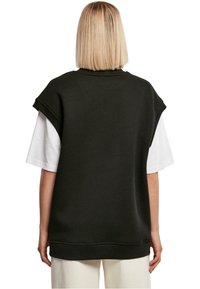 Musternike musta oversize-sviiter lühikeste varrukatega, valge T-särgi peal. Ümar kaelus ja soonikkoes serv. Lihtne, ühtlane disain.