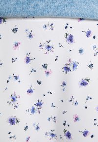 Tecido com padrão floral em azul e roxo sobre um fundo branco, coberto com material de malha azul claro. Textura suave.