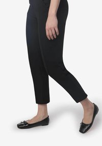 Pantalones negros de corte entallado y longitud hasta el tobillo, combinados con bailarinas negras con un acento de lazo y acabado brillante.