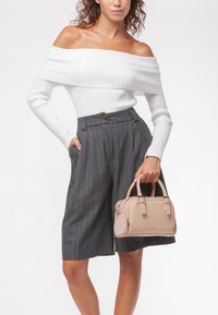 Borsa a tracolla in pelle beige con manici arrotondati e chiusura con zip, abbinata a una maglietta bianca a righe con spalle scoperte e pantaloni corti grigi a righe sottili a vita alta.