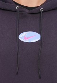 Hoodie roxo escuro com cordões pretos e um emblema oval azul com o logo da Nike em rosa no peito.