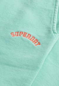 Miętowa bluza z haftowanym logo "SUPERDRY" w kolorze pomarańczowym. Miękka tekstura, okrągły dekolt i luźny krój. Prosty i minimalistyczny design.