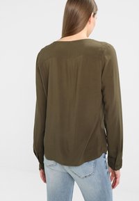 Olivgrön blus med lös passform, långa ärmar och rund hals. Slät tyg med en subtil lyster och knäppte manschetter.