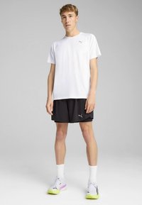 Valge lühikeste varrukatega spordisärk ümarkaelusega, millele on kombineeritud mustad lühikesed püksid. Komplektis on Puma logosid ning mitmevärviliste detailidega trennijalatsid.