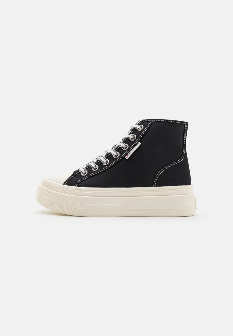 Black high-top sneakers with a canvas upper, white rubber sole, and silver eyelets. Features contrasting white stitching and a logo tag.