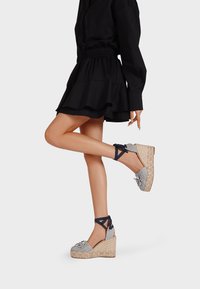 Sandali con zeppa e base in espadrilles intrecciata, parte superiore in tessuto blu e bianco, con decorazioni floreali e lacci incrociati alla caviglia.