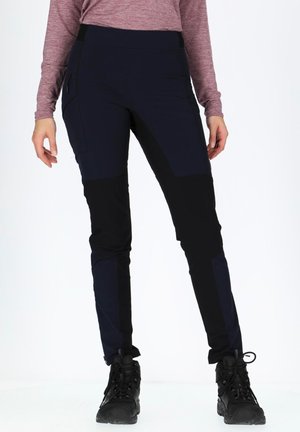 Navy and black hiking pants with a fitted design, featuring pockets and a stretchy waistband. Worn with black hiking boots on a light background.