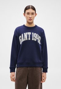 Tengerészkék pulóver "GANT 1949" felirattal krémszínben, lekerekített nyakkivágással. Hosszú ujjú és laza szabású. Puha tapintású anyag.