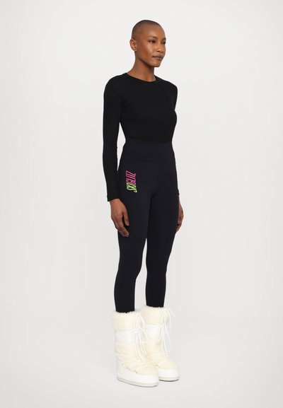 Fekete, hosszú ujjú, testhezálló felső, magas derekú fekete leggings-sel, amelyek színes logó részlettel rendelkeznek. A megjelenést fehér, szőrmés csizmák egészítik ki.