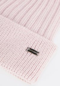 Bonnet rose tricoté avec une texture côtelée, comprenant des accents de fil argenté et un patch logo noir et argenté sur le revers.