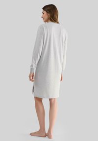 Camisa de noche de manga larga en gris claro con rayas blancas, fabricada en un tejido suave; presenta aberturas laterales y puños acanalados.