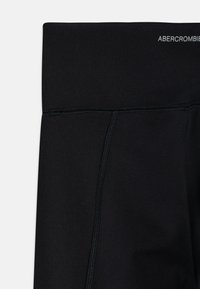 Leggings sportive neri con una consistenza liscia, caratterizzati da cuciture a contrasto e una vita con il logo "ABERCROMBIE" nella parte superiore.