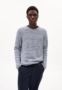 Hellblauer Rundhalsausschnitt-Pullover mit strukturiertem Strickmuster, kombiniert mit marineblauen Hosen. Der Pullover hat lange Ärmel und eine lockere Passform.