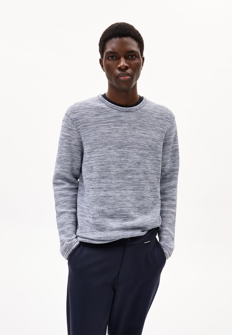 Hellblauer Rundhalsausschnitt-Pullover mit strukturiertem Strickmuster, kombiniert mit marineblauen Hosen. Der Pullover hat lange Ärmel und eine lockere Passform.