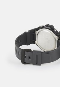 Montre en caoutchouc noir avec un bracelet texturé, un fond en acier inoxydable et un boîtier arrondi audacieux. Fermeture par boucle affichée sur le bracelet.