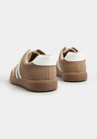 Sneakers sintetici marroni con accenti bianchi, caratterizzati da tre strisce, punta arrotondata e suola in gomma testurizzata. Il dettaglio del tallone posteriore è di un bianco liscio.