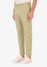 Pantaloni di cotone verde chiaro con vestibilità affusolata, tasche laterali e chiusura con bottone. Abbinati a sneakers bianche per contrasto.