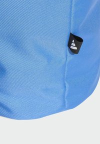 Blue fabric bag featuring a textured surface, rounded bottom, and a black tag with a white logo. Reinforced stitching along edges.