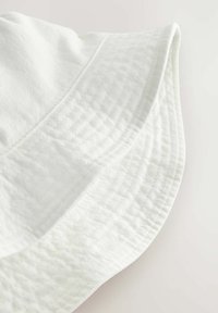 Weißer Baumwoll-Bucket-Hat mit strukturiertem Stoff, breiter Krempe und gestickten Details am Rand, der ein weiches, lässiges Design präsentiert.