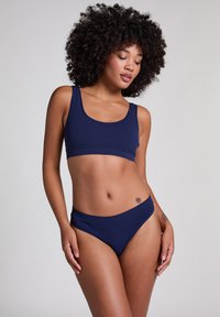 Meriininsininen ribbikoulu bikini-sarja, jossa on kaarrokehaukkasu ja korkea vyötärö. Sujuva pinta ja minimalistinen muotoilu ilman koristeita.