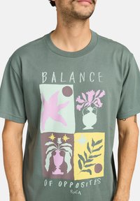 Green cotton t-shirt featuring a graphic design with pastel shapes, vases, and plants in yellow, pink, and light blue square sections.
