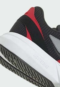 Čierna a červená športová obuv s priedušným sieťovaným zvrškom, textúrovanými prekrytiami, bielou medzipodošvou a patterned gumovou podrážkou.