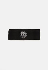Un bandeau en tricot noir avec un patch circulaire blanc portant le logo Emporio Armani EA7 au centre, représentant des montagnes et du texte.