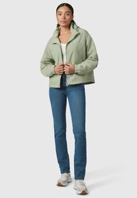 Light green, cropped jacket with a high collar and zipper closure, paired with blue jeans and gray sneakers.